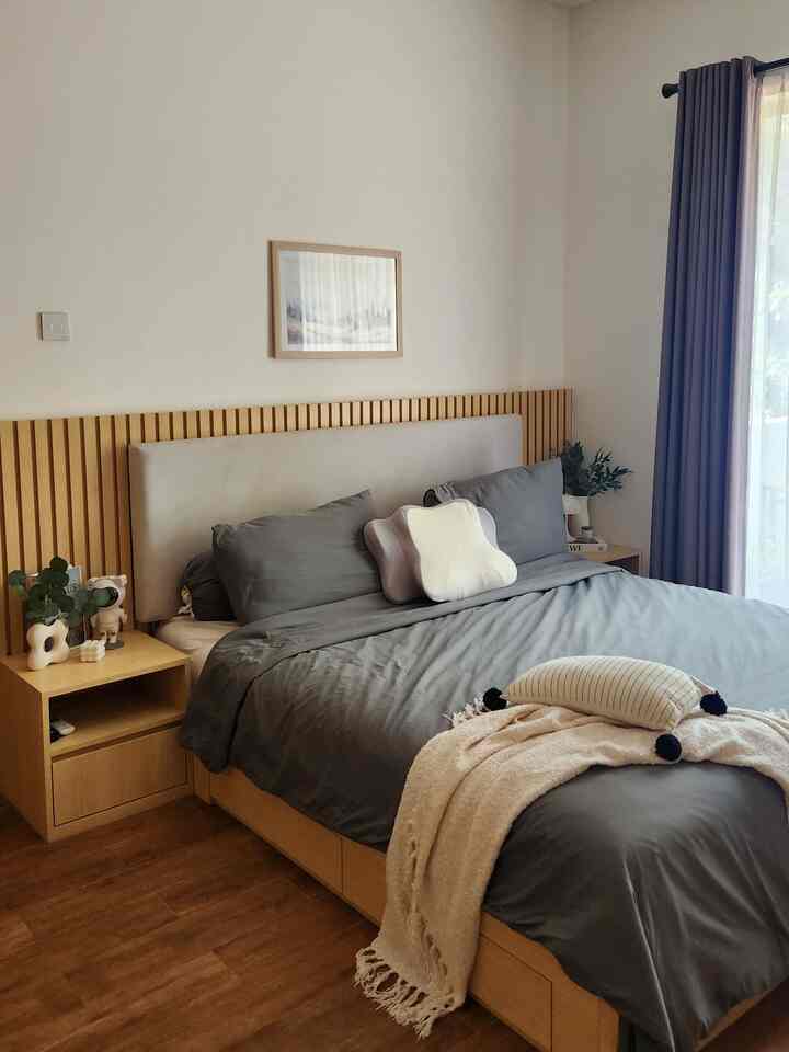 Natural-toned square bedroom with white walls, wood furniture, and grey bedding creating a calm and cozy atmosphere