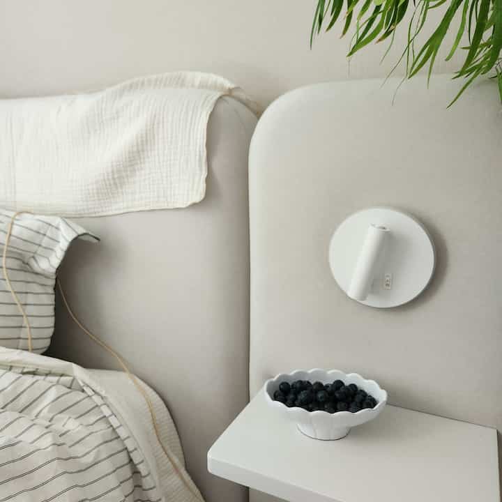 白とベージュのトーンの寝室、柔らかいファブリックのベッドフレームとスカラップの白い皿が配置されたシンプルでナチュラルな雰囲気のインテリア