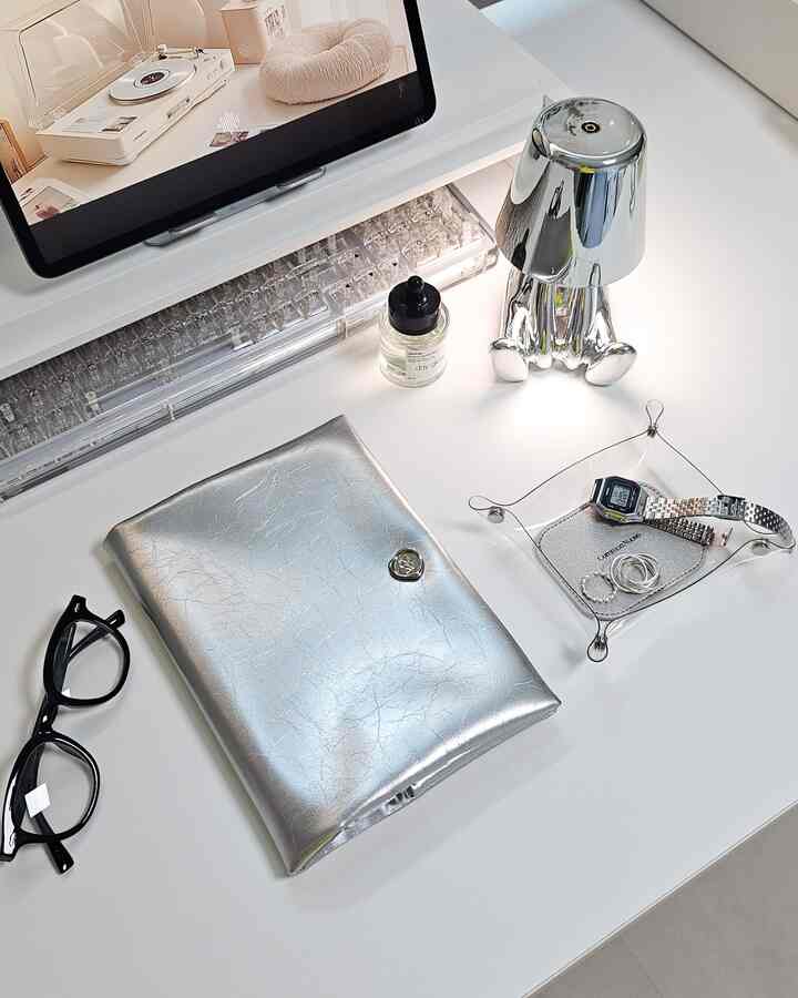 Bright white-toned desk featuring a silver diary cover, transparent tray, and digital devices arranged in a modern, tidy workspace