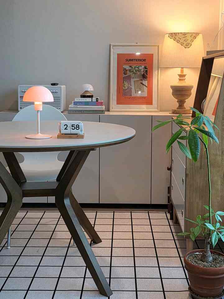 ナチュラルな色調のリビング・ダイニング、丸いダイニングテーブルとフロアランプ、フリップ時計、植物が配置された温かみのある空間