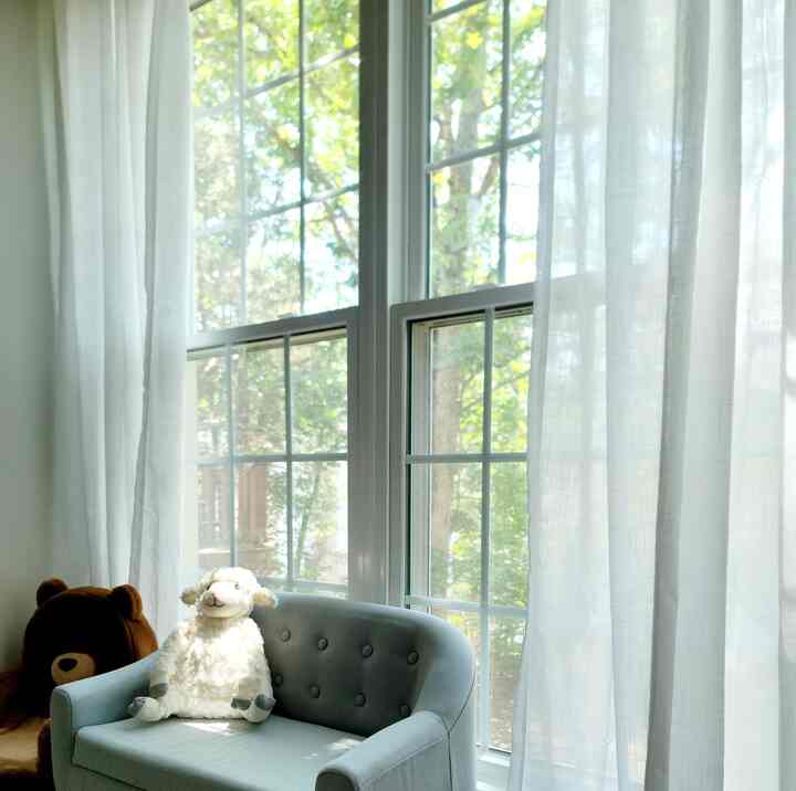 Natural-toned kids' corner featuring a small blue sofa, plush lamb, and sheer window curtains with sunlight pouring in
