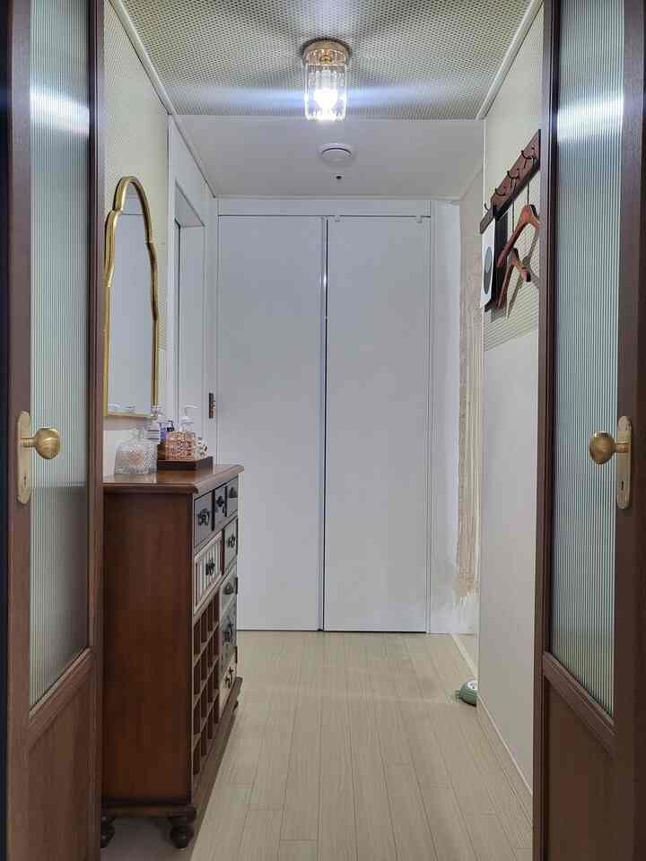 ゴールドのクラシックな化粧台と鏡が配置された狭く縦長の玄関スペース