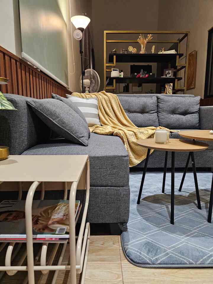A compact living room featuring a gray sofa and round wooden coffee tables with a yellow throw and floor lamp, creating a warm natural tone