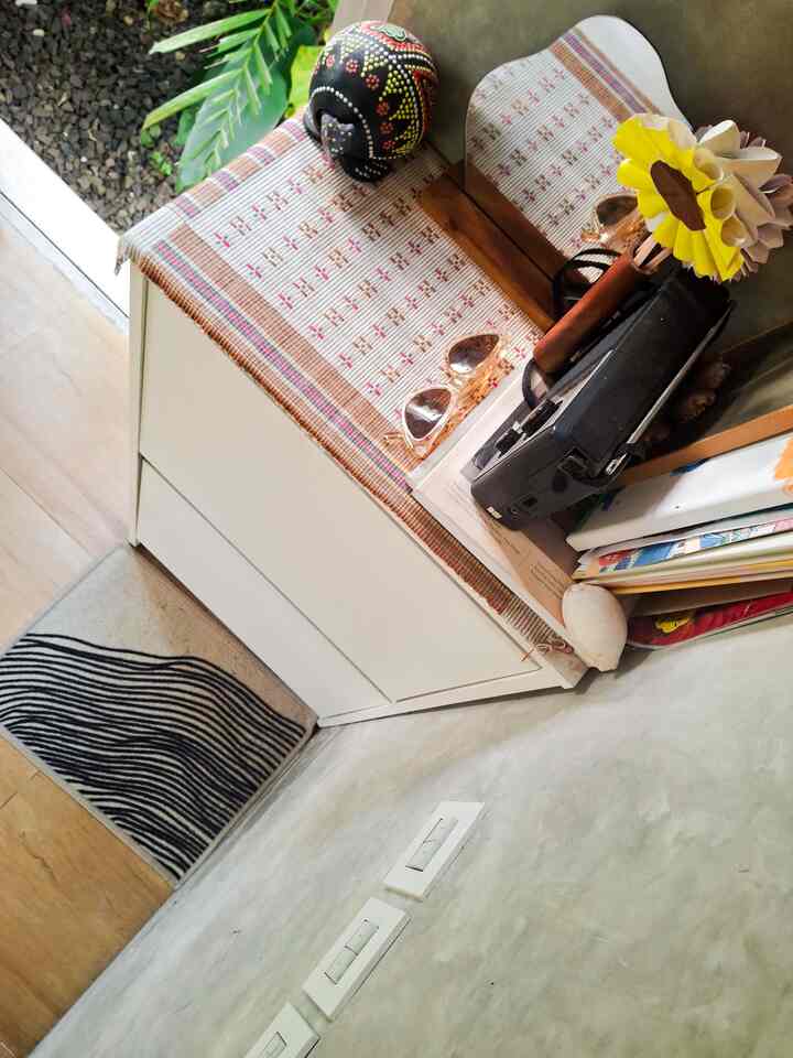 Natural toned entrance corner featuring a white storage cabinet with a fabric table runner and a nylon patterned floor mat, creating a cozy ambiance