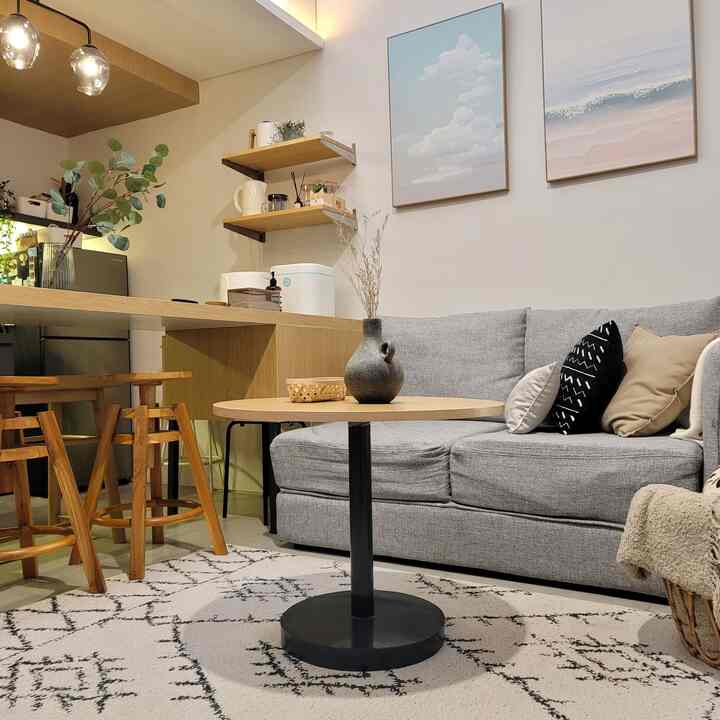Natural modern living room featuring a gray sofa and round wood coffee table centered. Wooden bar stools and wall art add cozy atmosphere.
