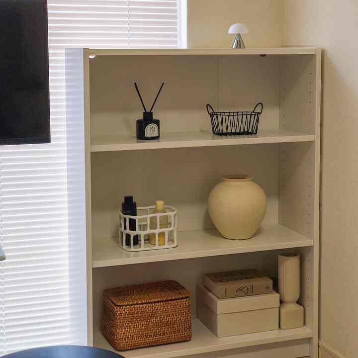 白を基調とした小さな部屋のコーナー、ラタンバスケットとセラミックの花瓶が置かれた収納棚が配置された、清潔感のある自然な雰囲気のインテリア
