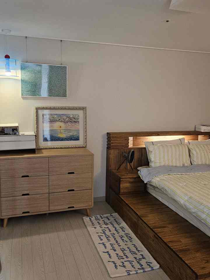 ナチュラルな木目と白い壁の寝室、シンプルモダンなスタイルで配置された木製ベッドフレームとチェストのある印象的な空間