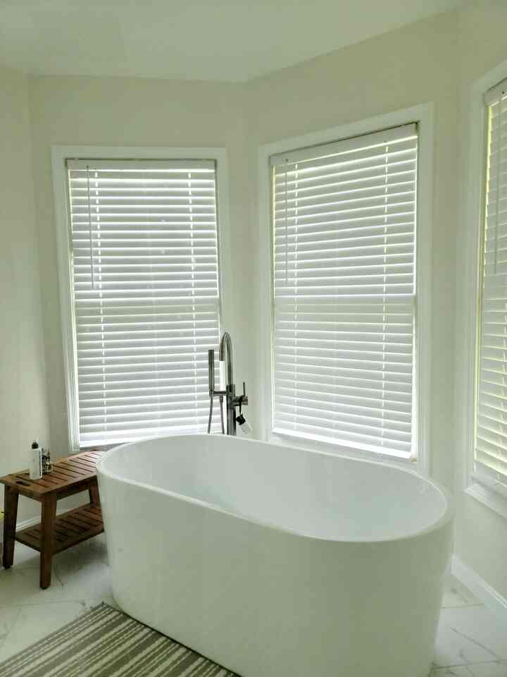 White and wood-tone bathroom featuring a central white bathtub and a wooden bench to the left in a clean space