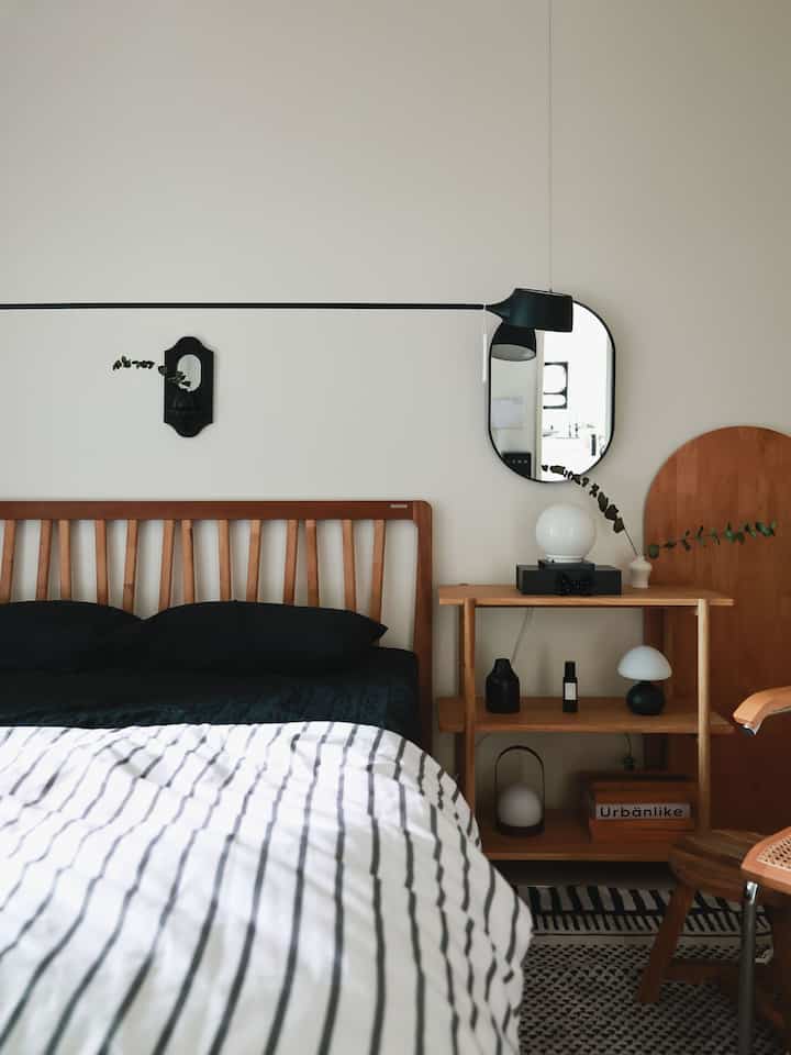 Natural wood tones and black accents create a clean bedroom space featuring a simple bed and storage shelf with cozy atmosphere
