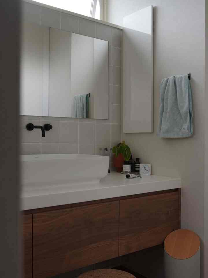 白とナチュラルカラーの調和がとれたバスルーム、木製キャビネットとタオルが置かれたシンプルな印象的な空間