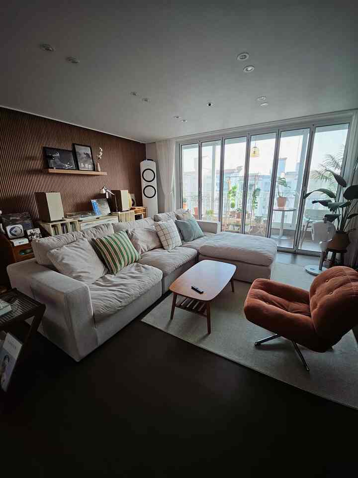 ナチュラルな木目調とベージュのソファがある二人暮らしのリビング、バルコニーの植物と落ち着いた雰囲気の空間