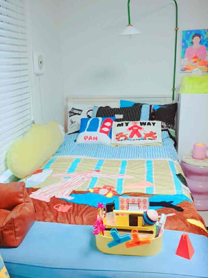 白を基調とした小さな寝室、中央にベッドと複数のクッションが配置されたシンプルな空間