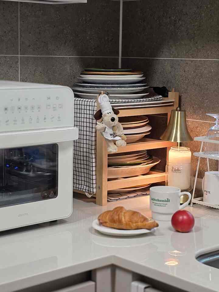 ホワイトとブラウンのトーンが調和したキッチン、皿やマグカップが整頓された木製ワインラックとカウンター上のコンパクトなオーブンが配置された雰囲気のあるインテリア