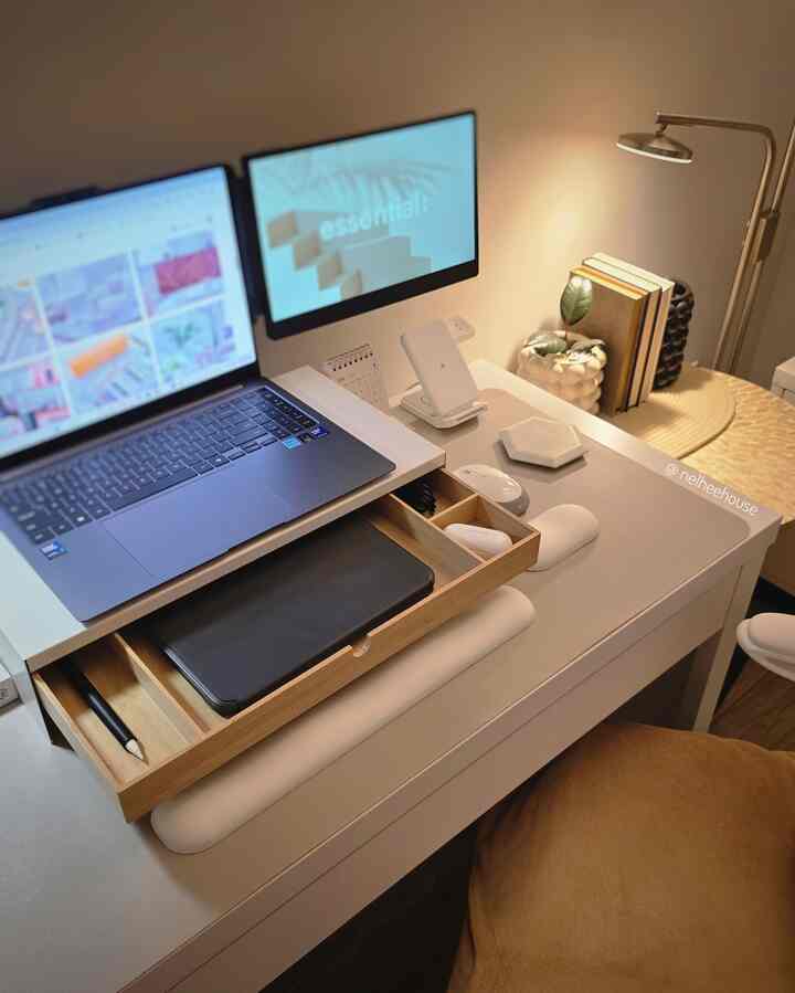 White and wood tone home office space featuring tidy desk, dual monitors, books, and a floor lamp creating a cozy atmosphere