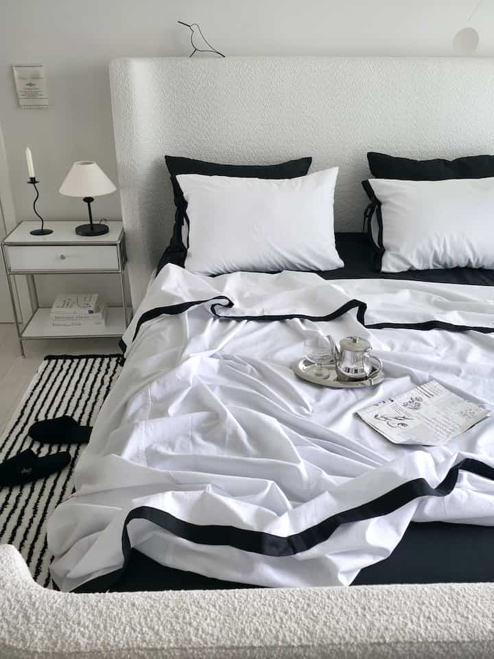 白と黒のモノトーンが調和した寝室、清潔感のあるファブリックベッドと整った寝具が配置されたモダンでホテルライクなインテリア