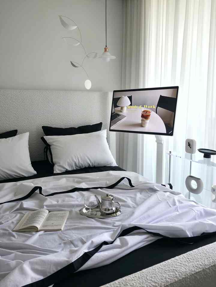 A clean and modern bedroom in white and black tones, featuring a functional workspace and reading area