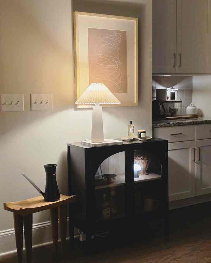 Cozy kitchen corner featuring white walls, black cabinet, wood-tone accents, and warm table lamp lighting