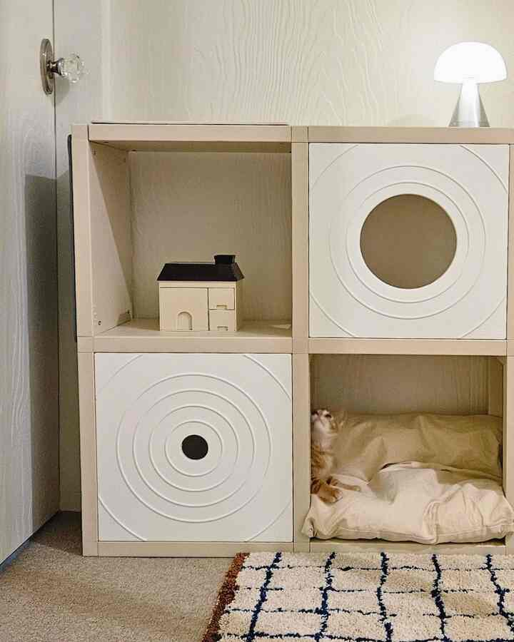 Beige-toned indoor cat tower with cushions creating a cozy space; an orange cat visible inside