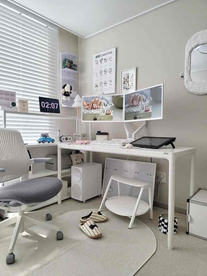 Bright home office in white and ivory tones featuring an organized desk with dual monitors and cozy cat accessories in a compact room