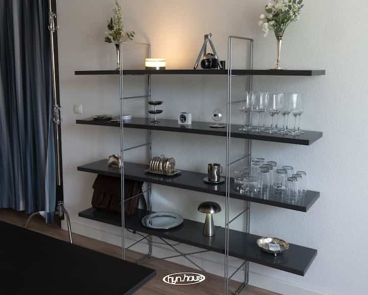 モノトーンのワンルーム、黒い棚とシルバーの装飾品が配置された落ち着いた実用的な雰囲気のインテリア