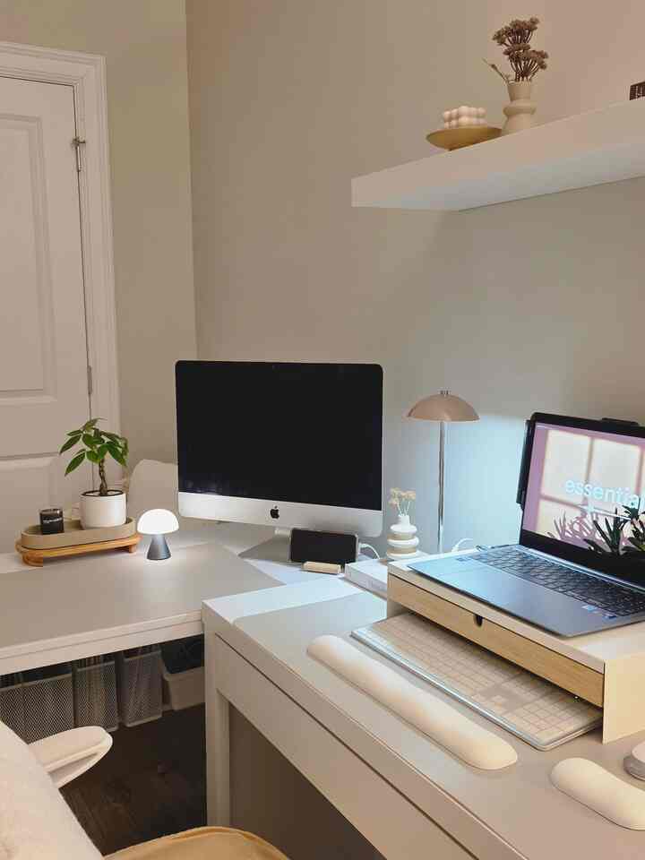 A compact home office space in white and natural tones, featuring a dual-monitor desk setup with a clean, minimalist atmosphere