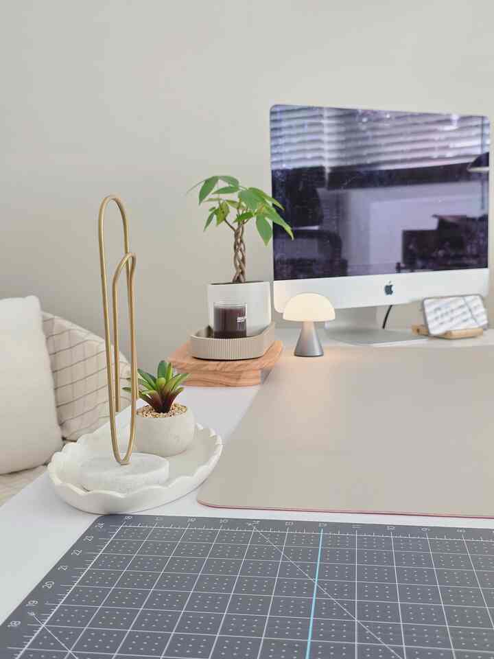 A simple modern home office with white and beige tones, featuring a desk with a monitor and plants arranged neatly