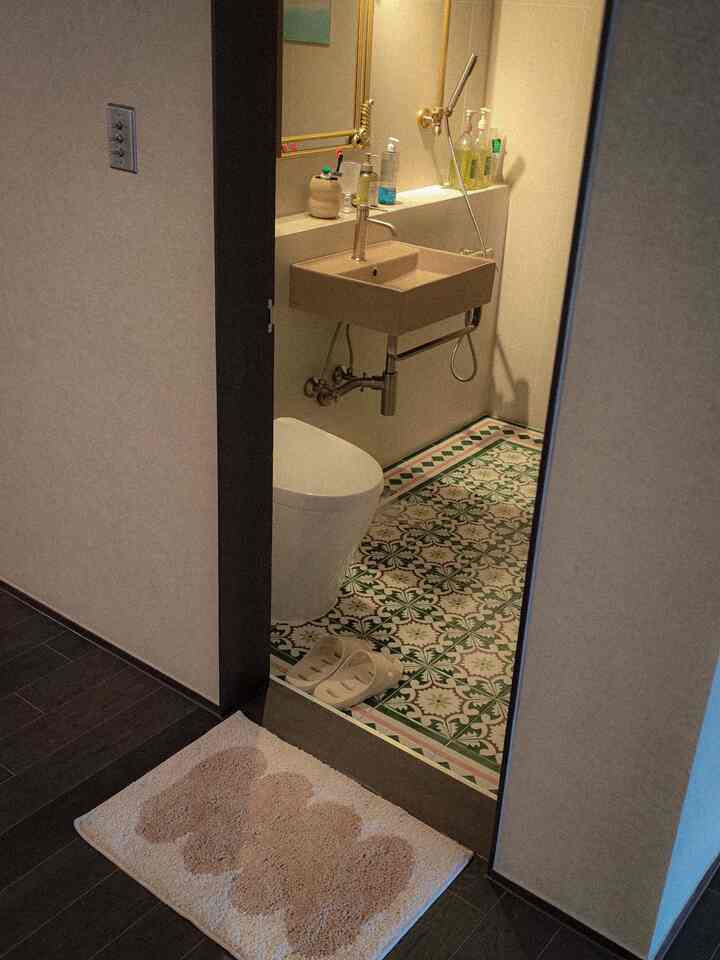 パターンの美しいヴィンテージタイルの床とブラウンの洗面台、白い便器が配置された温かみのあるバスルーム