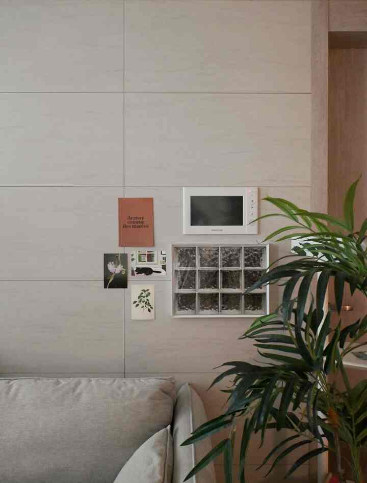 ベージュのタイル壁とベージュソファが配置された、ネコのアートや額縁があるナチュラルスタイルのリビングスペース