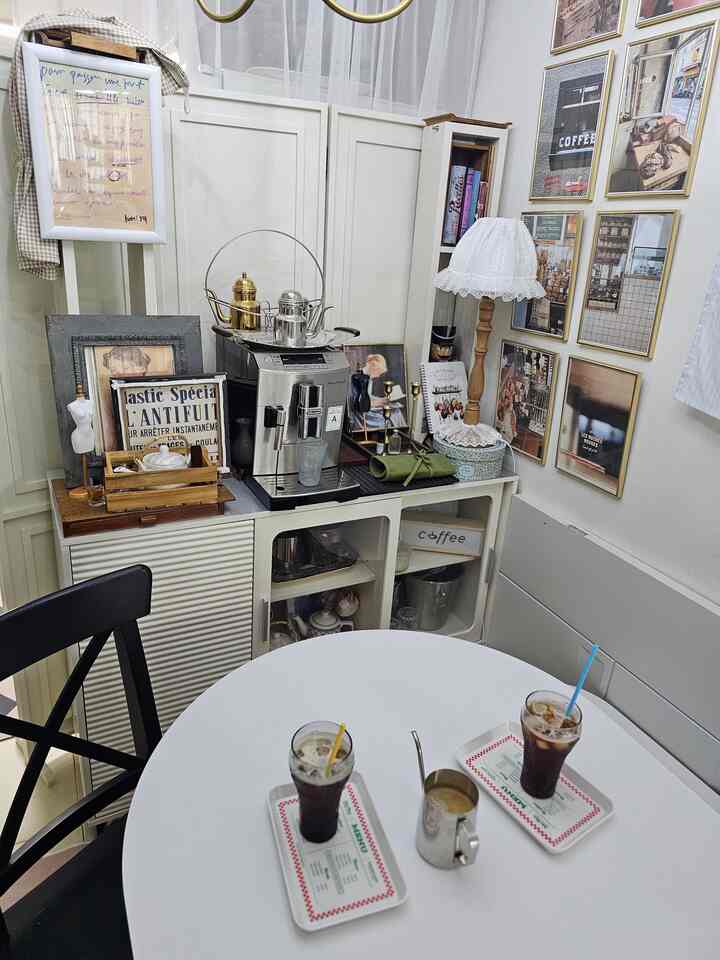 ホワイトと木目調が調和したヴィンテージ風のおうちカフェ空間、コーヒーマシンとヴィンテージの額縁が配置された温かなキッチンインテリア