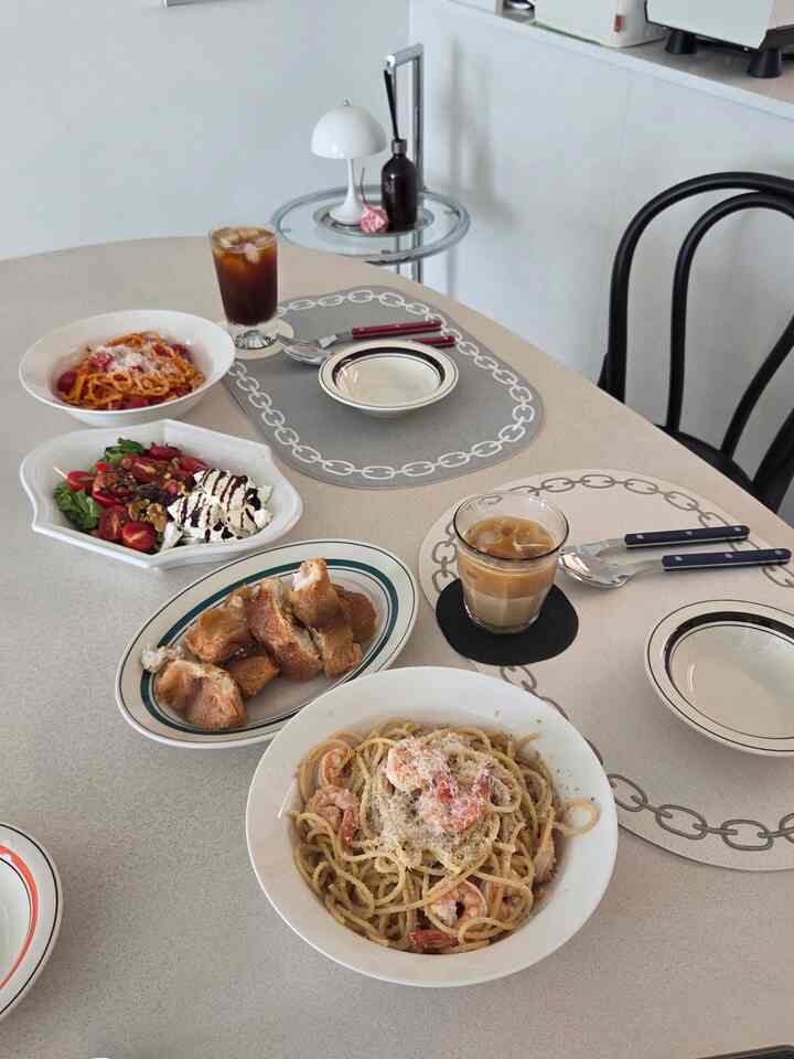 ベージュトーンのダイニングルーム、ダイニングテーブルと椅子にパスタ、サラダ、パンと飲み物が配置された雰囲気のある空間