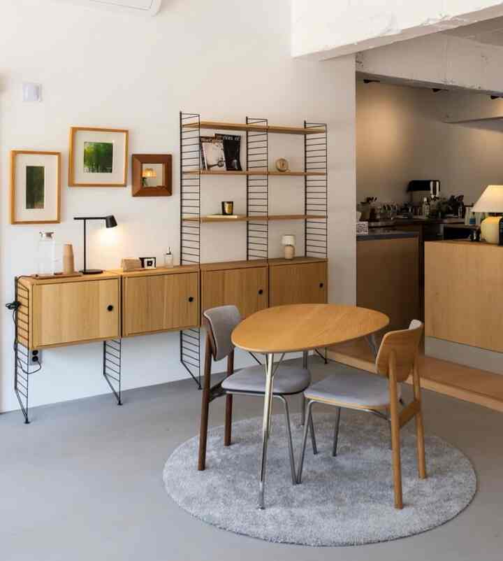 A simple dining room with natural wood tones and white walls, featuring a round table and shelves creating a cozy atmosphere.