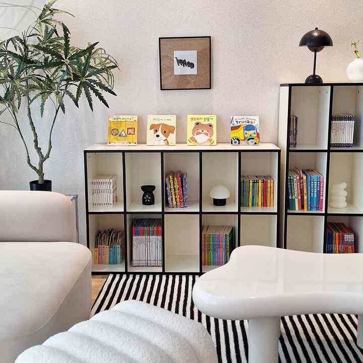 白と黒の色調のリビング、全面本棚とコーナーソファ、ストライプのラグが配置されたミッドセンチュリーモダンなインテリア