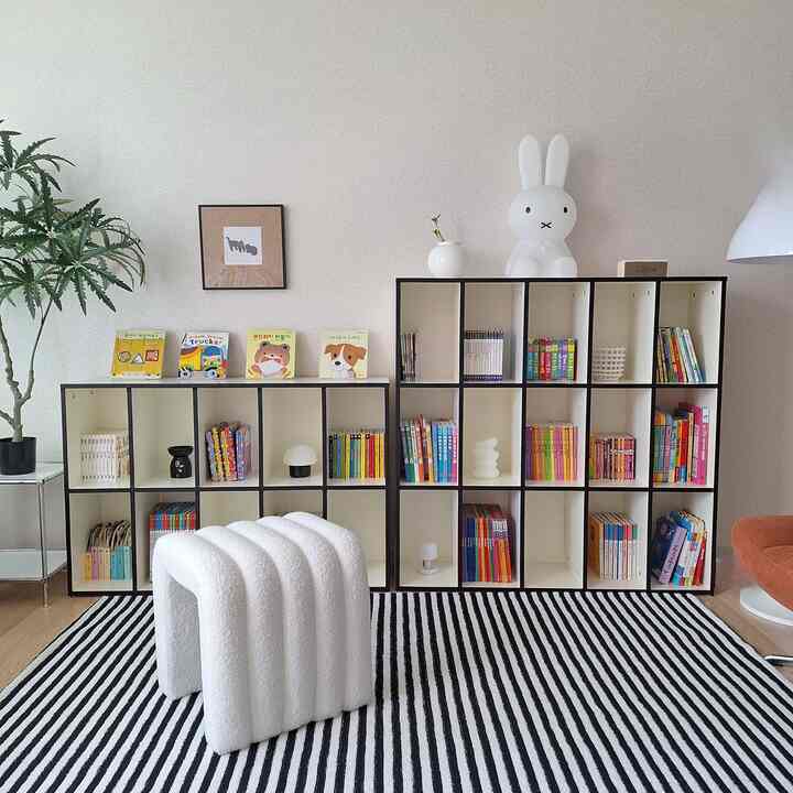 白とナチュラルカラーの子供部屋、本棚とかわいいウサギのムードランプ、白黒のストライプラグが配置された印象的な空間