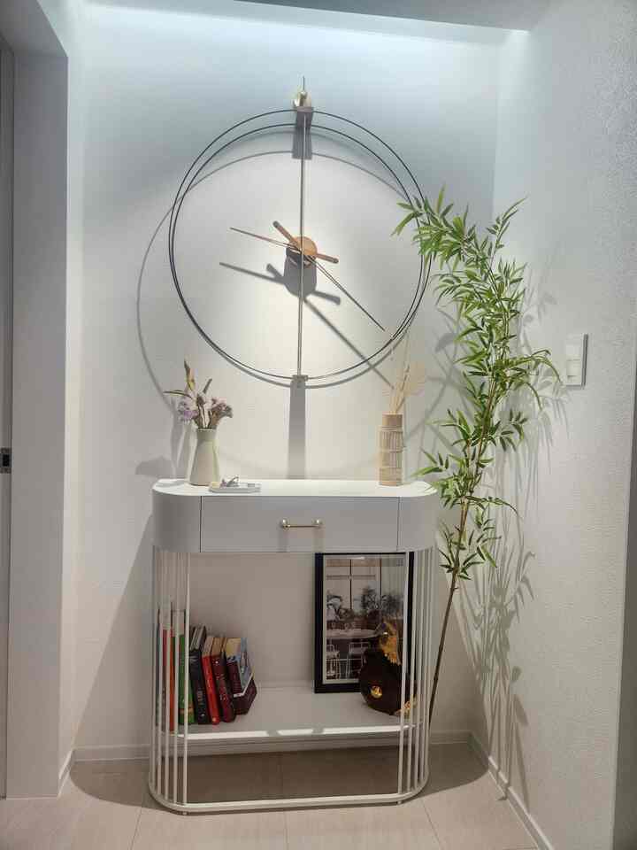 White-toned narrow space beside walk-in closet featuring a round console, large wall clock, and plant in a clean interior