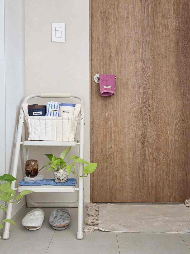 白と木目調が調和するバスルーム前、ラダーにファブリックバスケットとタオル、植物が配置された印象的な空間