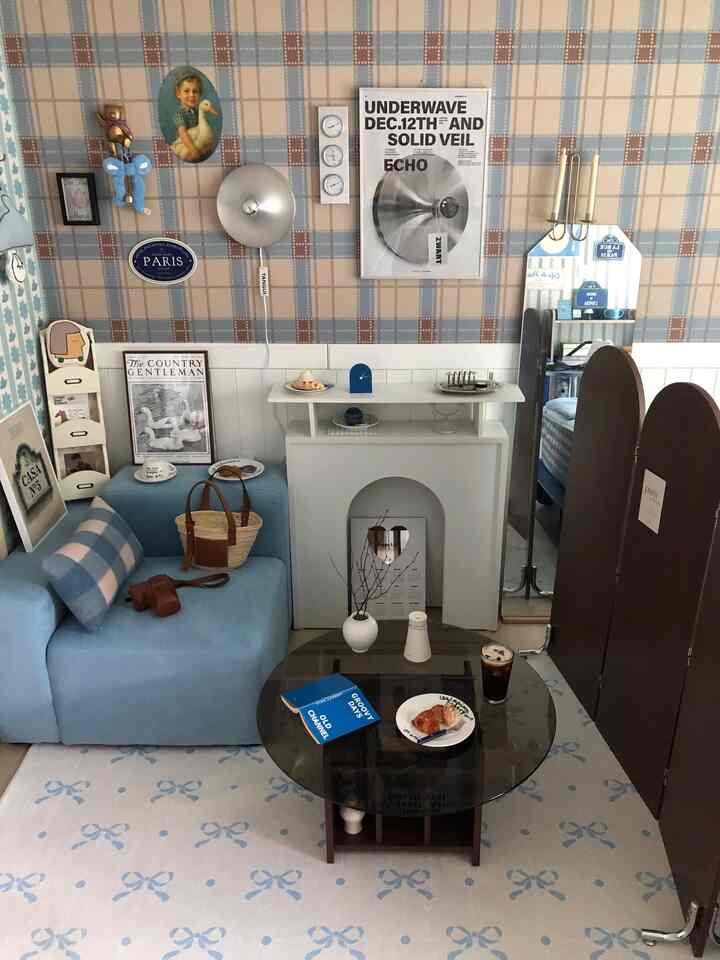 ナチュラルな色調のワンルームリビング、パステルブルーのソファとラグ、ポスターが調和した印象的な空間