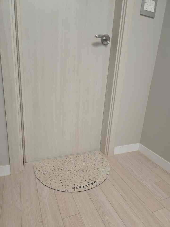 白いトーンの玄関、半円形のバスマットが配置されたシンプルで統一感のある空間