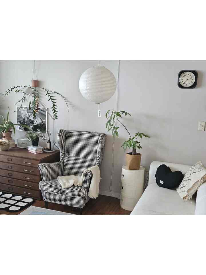 モノトーンのリビング、ハウンドトゥース柄のウィングチェアとホワイトソファ、多数の植物が置かれたシンプルなインテリア