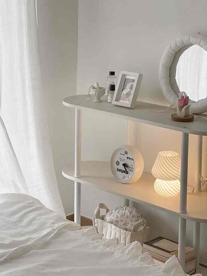 White and natural toned bedroom featuring round storage shelf with cozy lighting and simple decor atmosphere