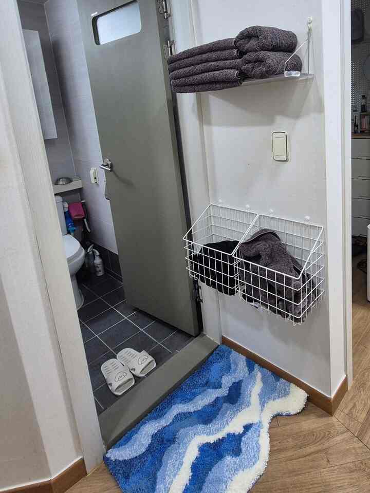 白い壁と青いバスマットのある浴室入口の空間、タオルと棚が整った雰囲気のあるインテリア