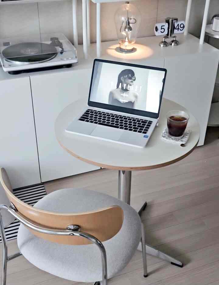 A compact space in white and wood tones featuring a round table, chair, laptop, and table lamp creating a minimal home office setup