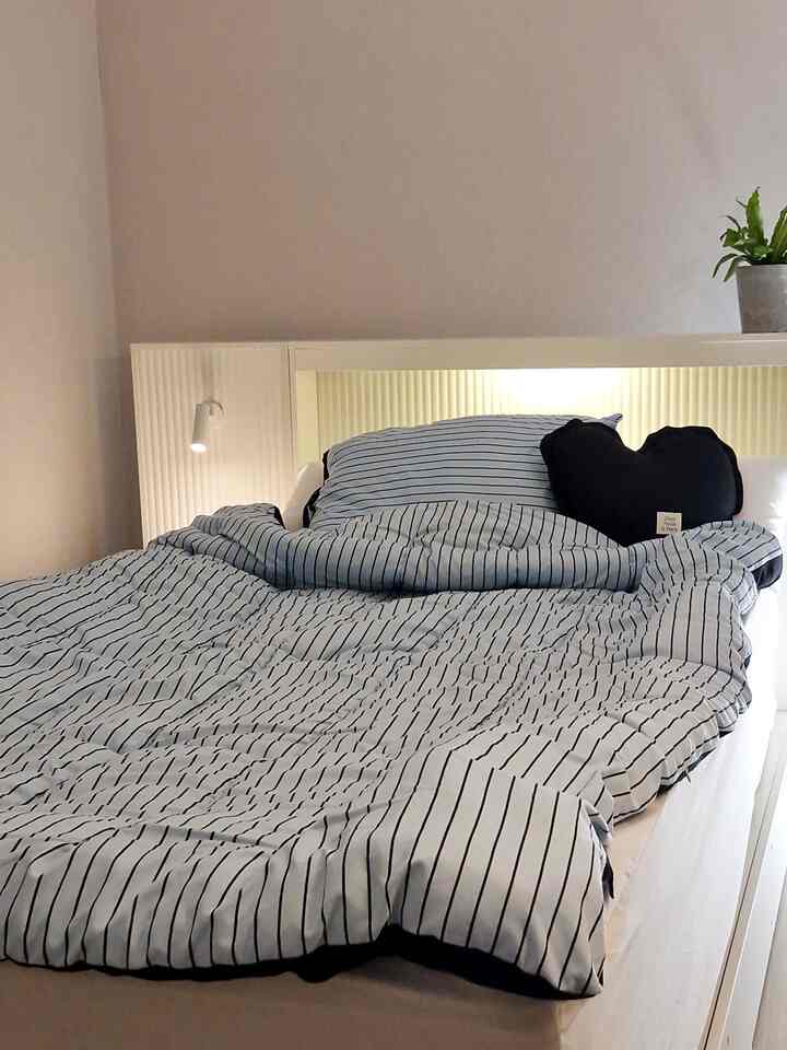 Cozy bedroom featuring a white bed frame with navy striped duvet cover and a black heart-shaped cushion
