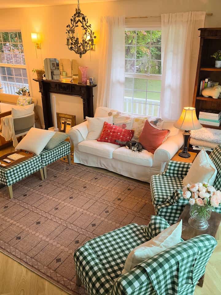 ホワイトとグリーンの色調のリビングルーム、広いソファとチェック柄のアームチェアが配置された田舎風の雰囲気のあるインテリア