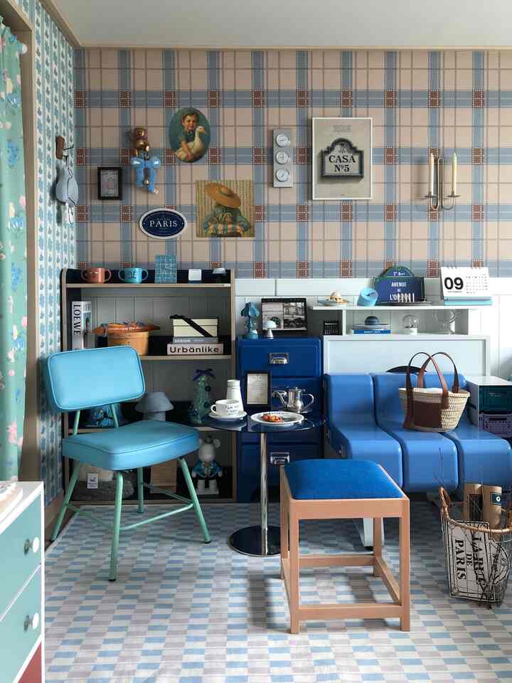 青と白のトーンのリビングルーム、ヴィンテージポスターとブルーのソファ、スツール、小さなテーブルが配置された雰囲気のあるインテリア