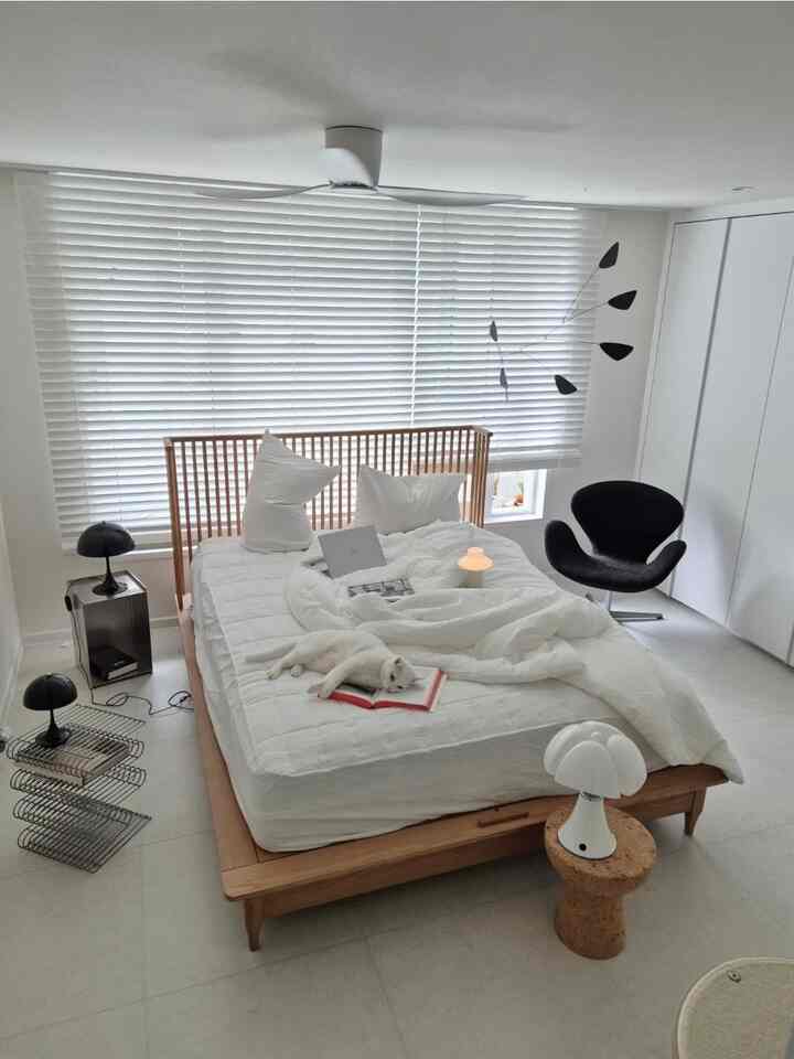 ホワイトとナチュラルウッド調が調和する寝室、すっきりとしたベッドに猫がくつろぐ雰囲気のあるインテリア