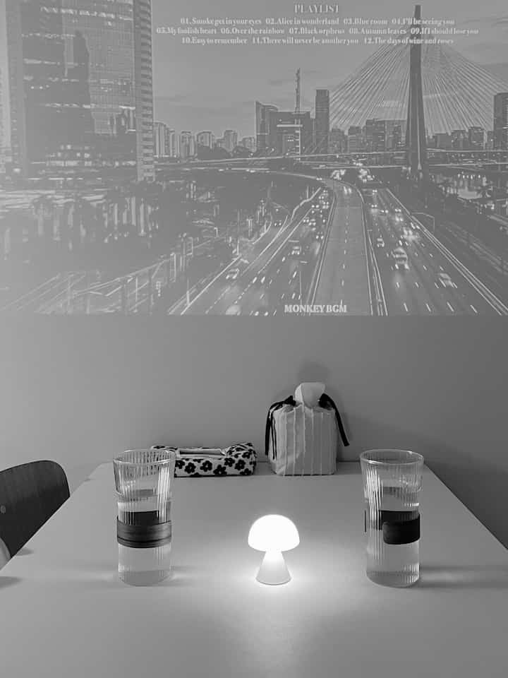 White-toned dining room featuring a clean dining table with a mini LED mushroom lamp and tissue covers in a minimalistic setting