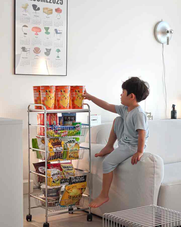 白いトーンのリビングルーム、ベージュのソファに子供が座り、お菓子でいっぱいの透明なワイヤー収納ラックが配置された雰囲気のあるインテリア