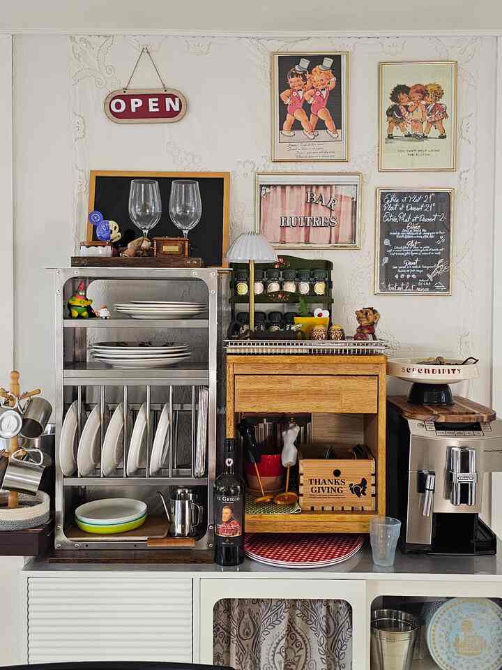 White-walled kitchen space featuring wood-tone storage unit, vintage framed art, and a coffee machine creating a home cafe ambiance