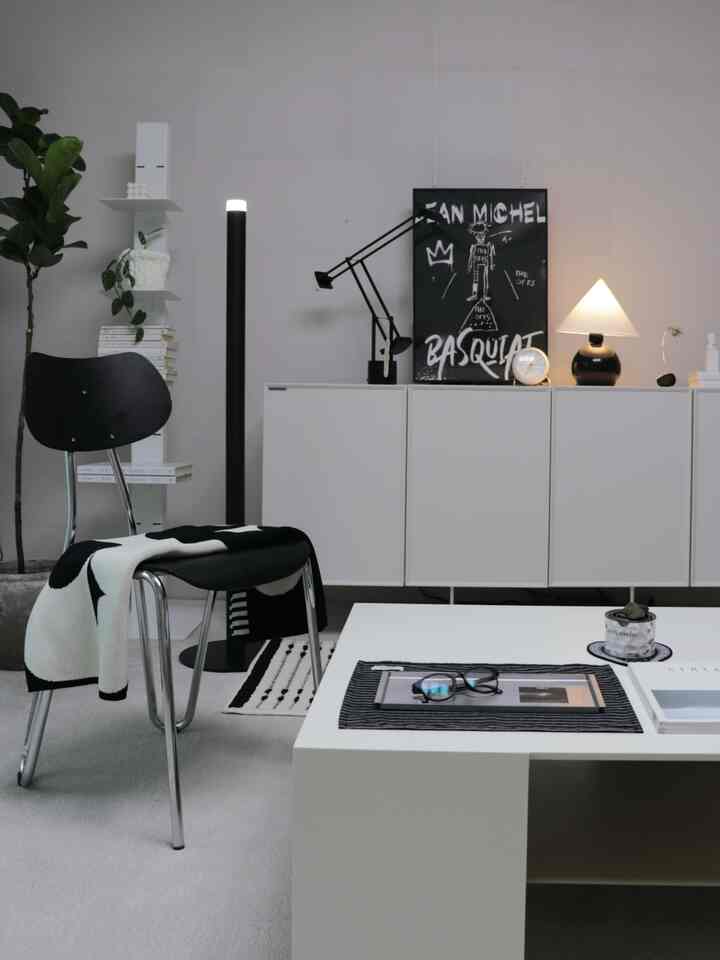 A natural modern living room in white and black tones featuring a white storage cabinet, black chair, and table lamp with a clean aesthetic