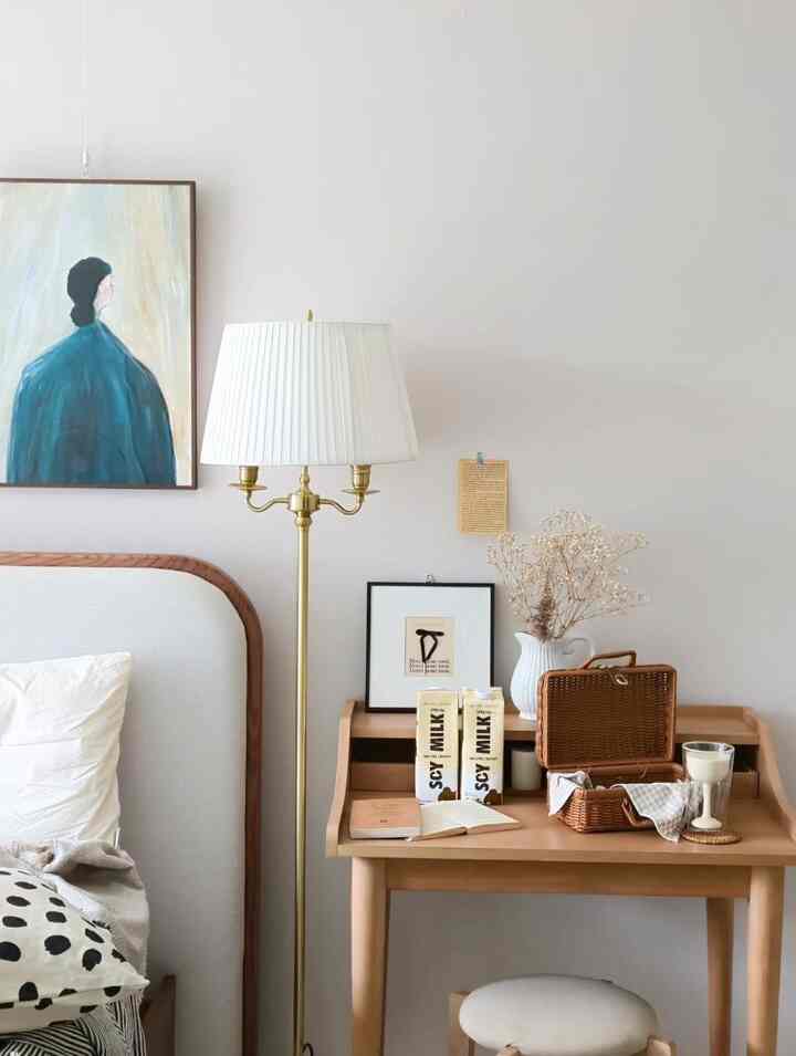Beige and white toned bedroom featuring wooden furniture, floor lamp, and picture frames with a cozy natural atmosphere